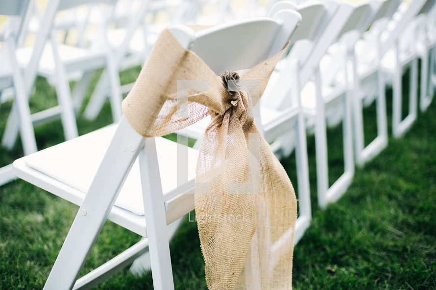 burlap ribbon around white folding chairs for an outdoor wedding 