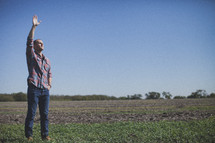man in a field raising his hand in worship 