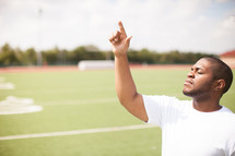 man on a football field pointing up to God 