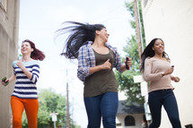teen girls running down a street carrying cellphones 