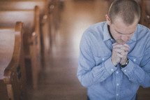 man kneeling in prayer in the aisle of a church