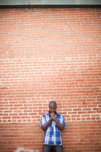 an African American man praying in front of a brick wall 