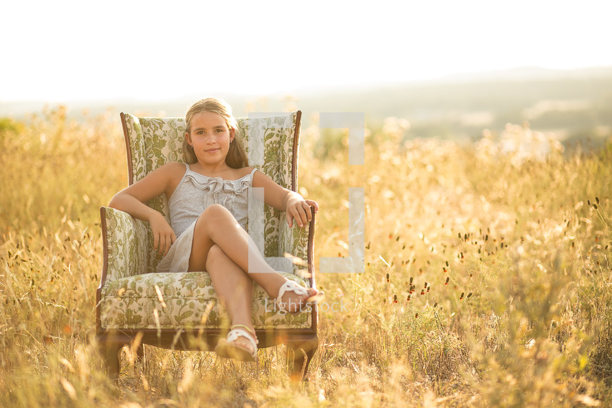 young girl sitting in a chair in a field