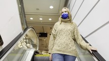 Woman wearing a face mask riding an escalator at a mall.