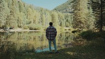 a man standing in a forest by a lake 