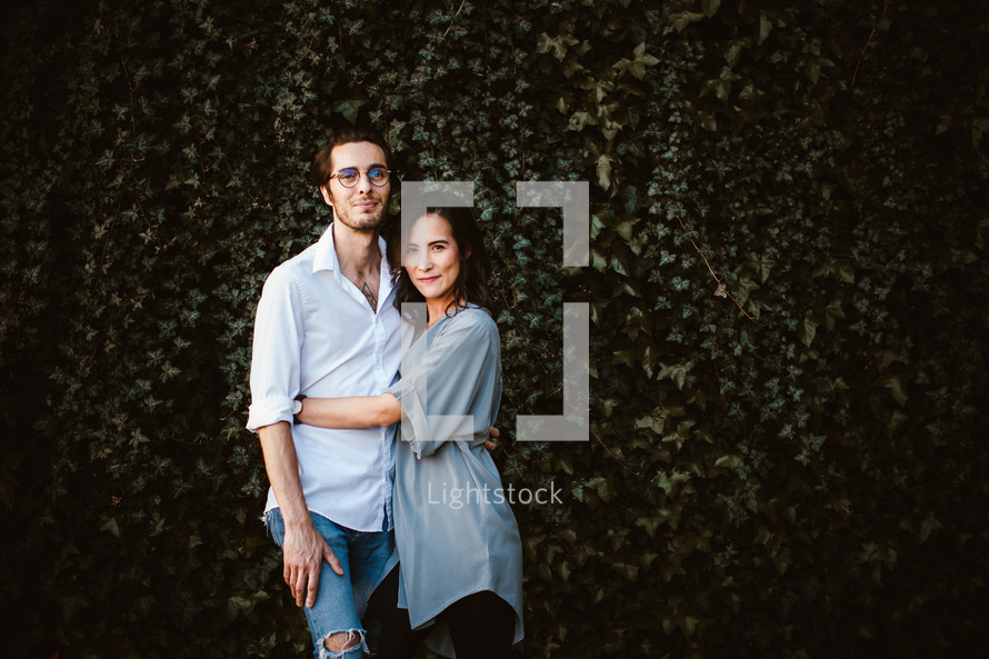 a couple standing together in front of an ivy covered wall 