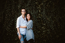 a couple standing together in front of an ivy covered wall 