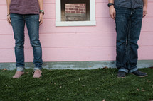 Man and woman standing in grass beside window on pink house.
