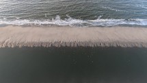 Aerial, tilt down, drone shot towards small waves hitting a beach, at the North sea, on Langeoog island, in North Germany