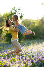 mother holding and swinging her child in a field of blue bonnets