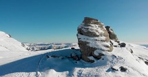 Aerial, rising, drone shot tilting over the sphinx rock formation, on the top of the southern Carpathians on a sunny winter day, in the Bucegi Natural Park, Romania