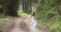 Young beautiful woman with a white dress walking in a green forest