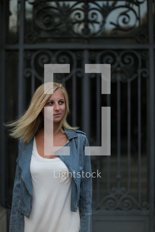 blonde woman with her hair blowing standing in front of a gate