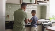 Son helping his single  father to wash the dishes.