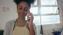 Young beautiful African-American woman standing by kitchen stove, cooking food at home, smiling and talking on cell phone. Tilt-up shot
