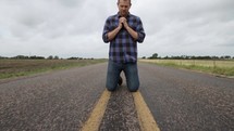 man in prayer on the center lines of a lonely road 