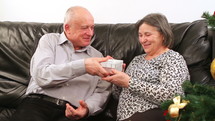 Elderly couple talking near a Christmas tree and exchanging gifts 