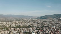 Long linear streets with large residential areas in the city of Oaxaca which is hemmed in by the green mountains of the southern Sierra Madre on a sunny day. Wide drone panning shot