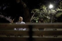 couple sitting on a park bench at night looking at each other 