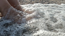 Woman's feet on a pebble beach with waves washing over them