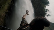 Close up of mans Hand Reaching Toward Pailon del Diablo Waterfall In Baños de Agua Santa, Ecuador.