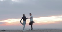 Young people in headphones exercising on the beach