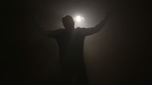 a man with raised arms in payer and worship in hazy light 