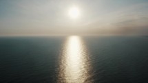 Drone view of an ocean glistening in the light of the sunset.