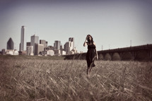 woman standing in a field in front of a city