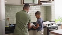 Son helping his single  father to wash the dishes.
