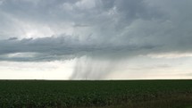 Rainfall in stormy, cloudy sky on farmland in the summer. Raining from storm clouds on crops, grassland in farming community during thunderstorm in cinematic slow motion.