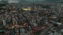 Aerial panorama over cityscape of Quito Downtown with high-rising buildings surrounding soccer stadium during cloudy day in dusk - Quito City,Capital of Ecuador