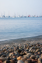 stones and rocks on the shore of a beach by the ocean in Lima Peru with boats in the distance