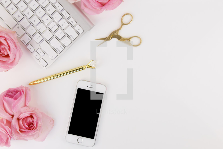 pink roses, pen, scissors, keyboard, and cellphone on a desk 