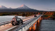 suv crossing bridge with snow capped volcanoes in the background at sunset 4K