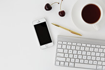 iPhone, computer keyboard, gold pen, cherries, and cup of coffee 