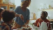 Young Black woman cutting sweet cake into pieces while taking care of family members during holiday celebration at home
