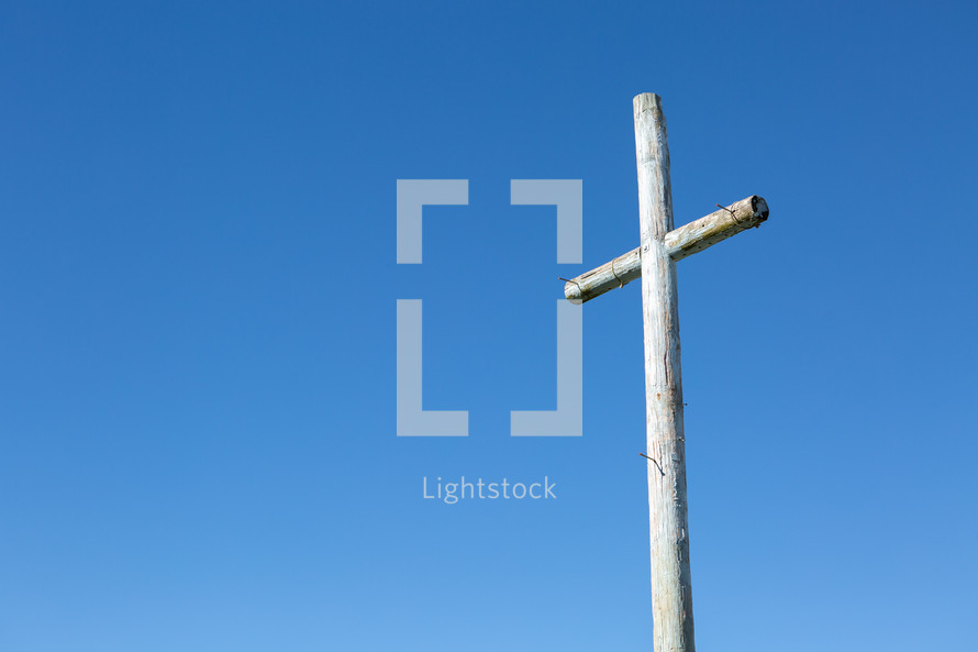 Rustic wooden cross with nails against blue sky 