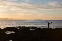 a person standing on a shore with arms raised 