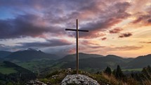 Christian cross in beautiful mountain nature, at sunset, clouds colored in pastel colors in spring