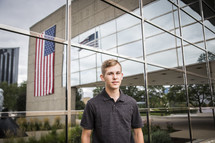 reflection of a large American flag and teen boy standing in front 