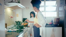 Young African-American mother cooking food on gas stove and speaking with cute little daughter sitting on kitchen countertop. Family life, happy parenthood concepts
