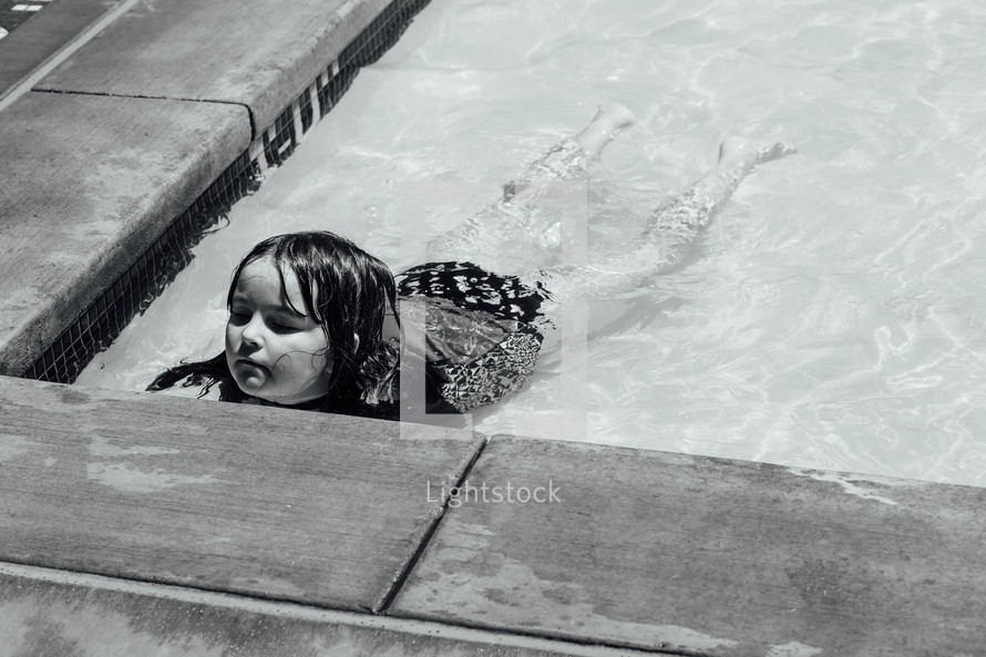 a little girl wadding in shallow water in a public pool 