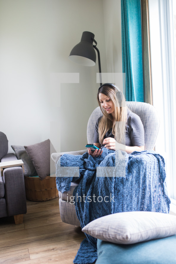 a woman sitting in a chair listening to a Bible app with headphones 