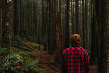 a man in a plaid shirt standing in a forest 