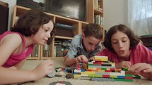 Three kids playing with toy plastic bricks at home