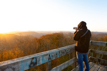 Photographer taking pictures of sunrise and autumn forest atop Bickle Knob wooden watchtower outlook in West Virginia 
