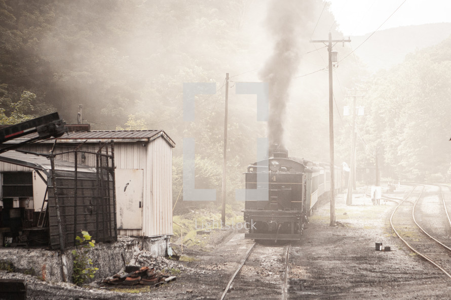 Smoky train engine on tracks passing old shed
