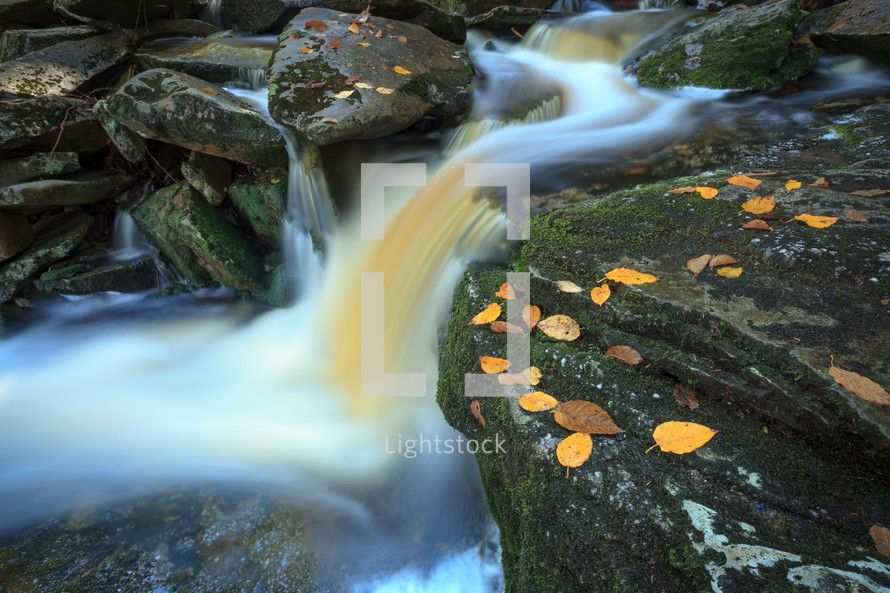 Fast waterfall flowing down rocks with autumn leaves slow shutter speed