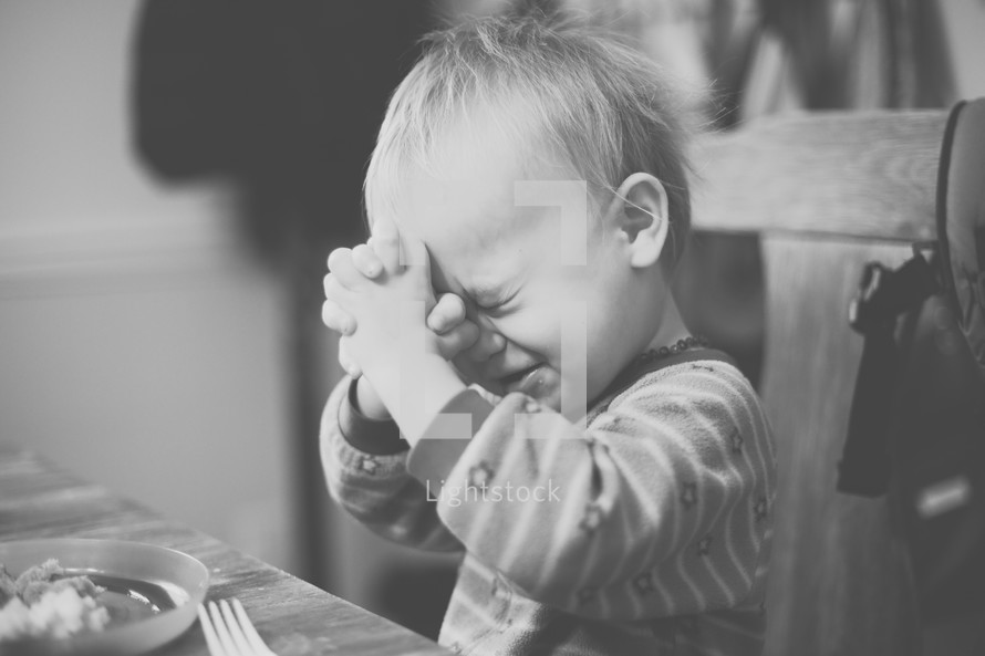toddler boy with praying hands at the dinner table 